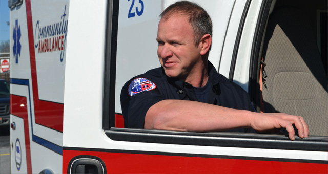 Paramedic standing on the passenger side of a Community Ambulance vehicle looking off into the distance